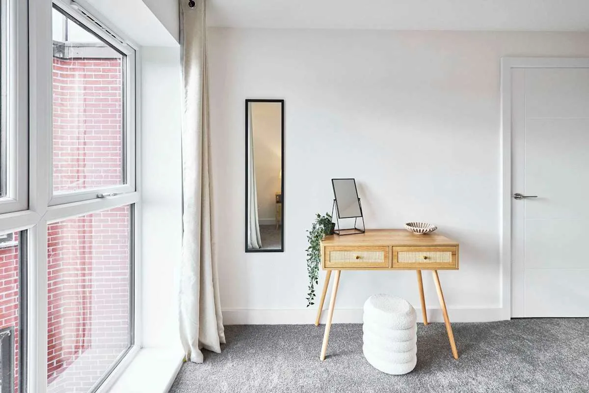 A bright room with a wooden desk, mirror, and large window.