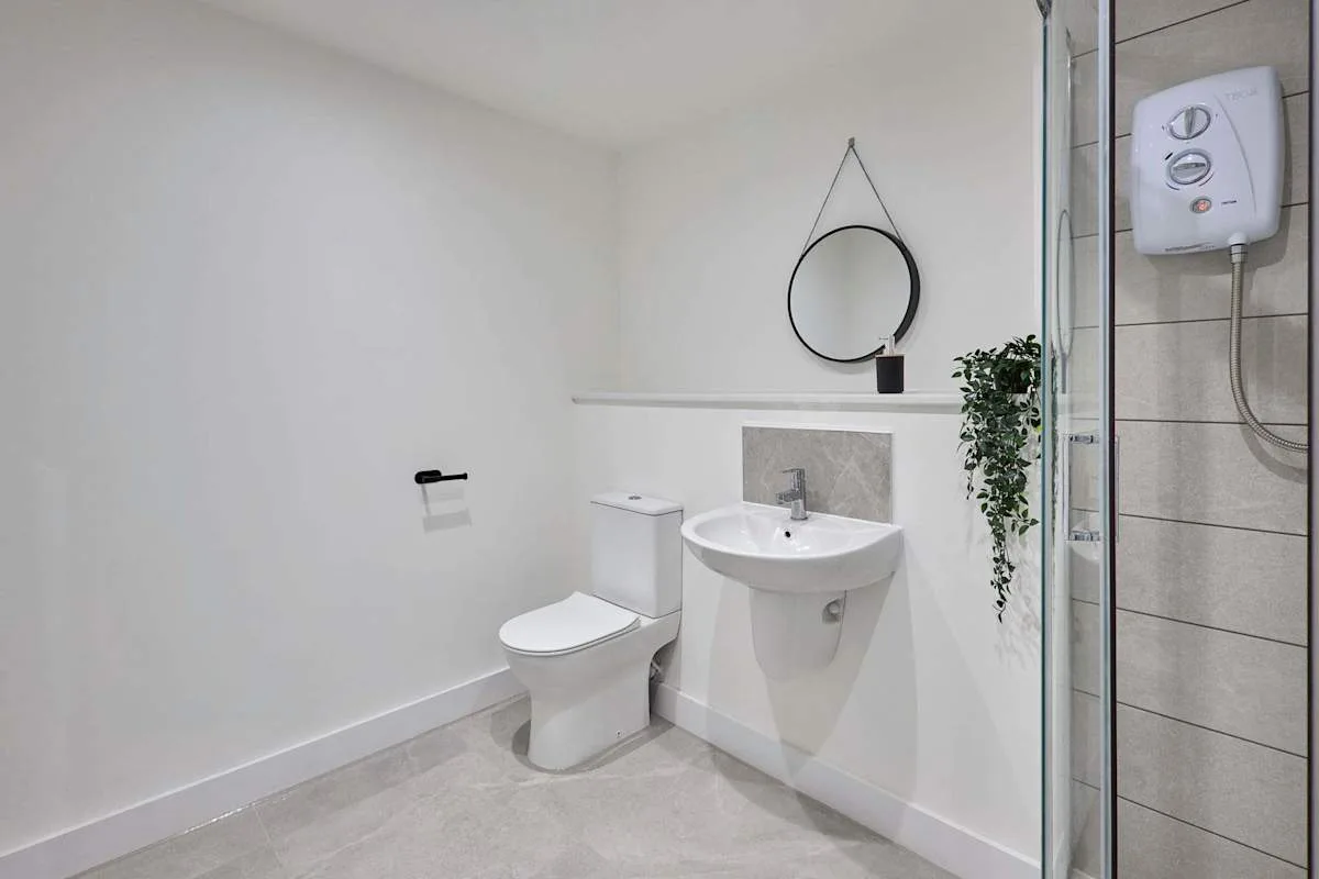 A bright bathroom with a toilet, wall-mounted sink, and round mirror.