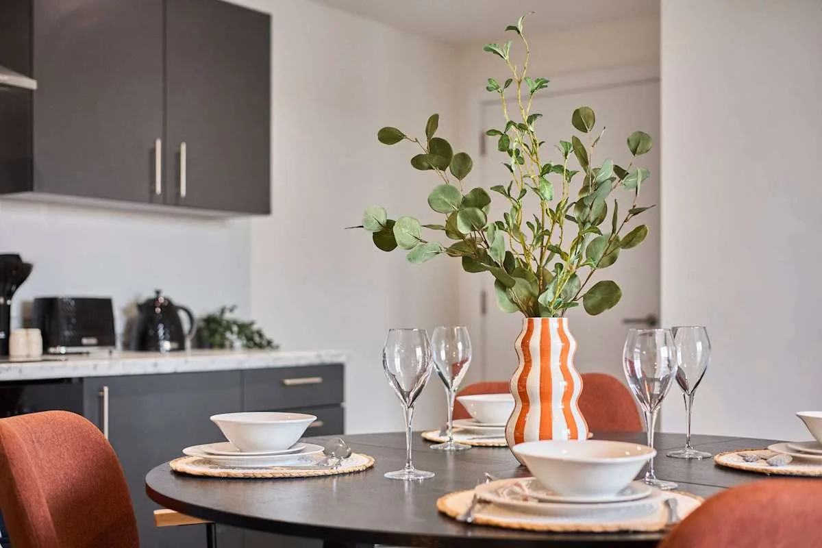 A dining table is set with dishes and a vase of leafy branches.