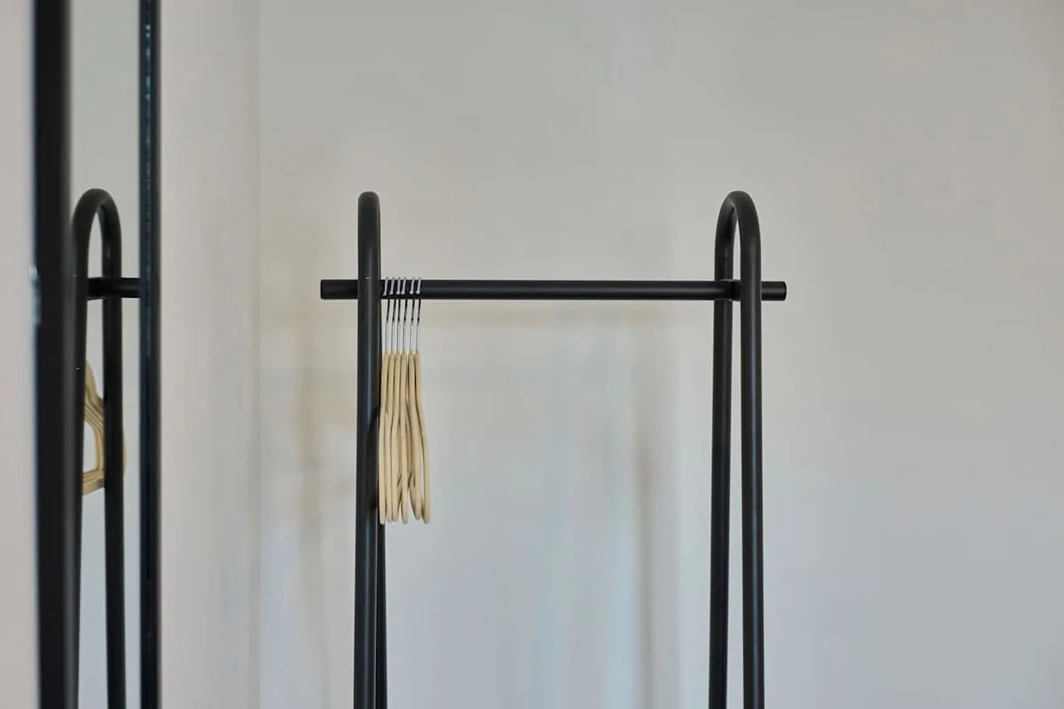 A clothing rack with wooden hangers stands beside a full-length mirror.