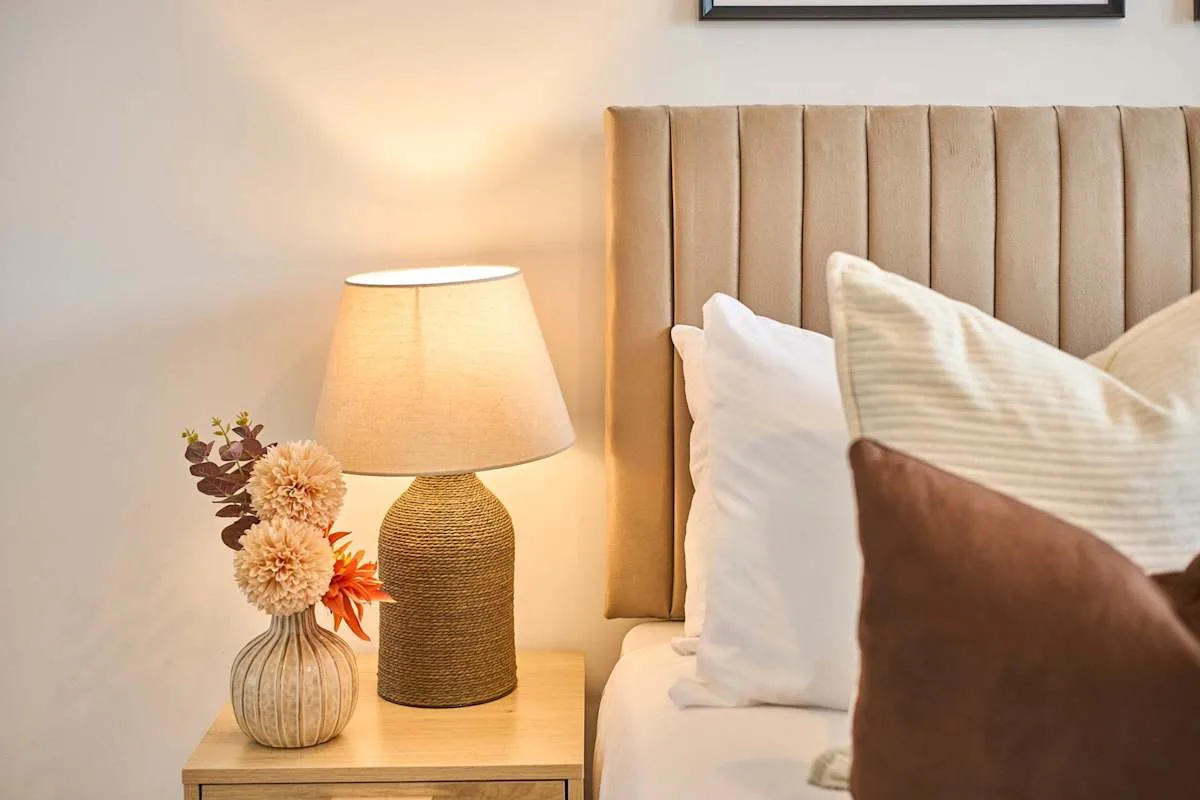 A bedroom with a tall upholstered headboard and a bedside lamp.