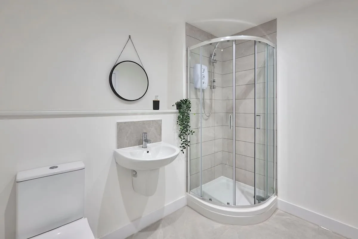 A bathroom with a wall-mounted sink and curved glass shower.