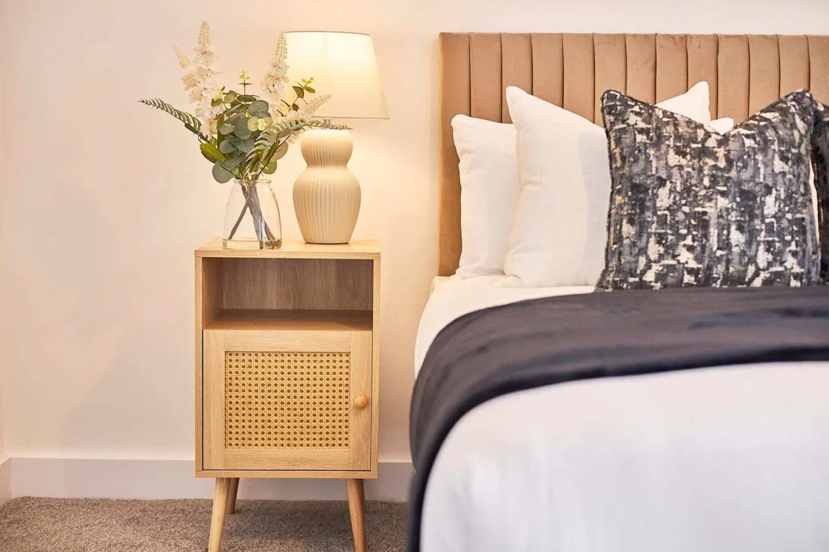 A bedroom with a bed beside a wooden nightstand and lamp.