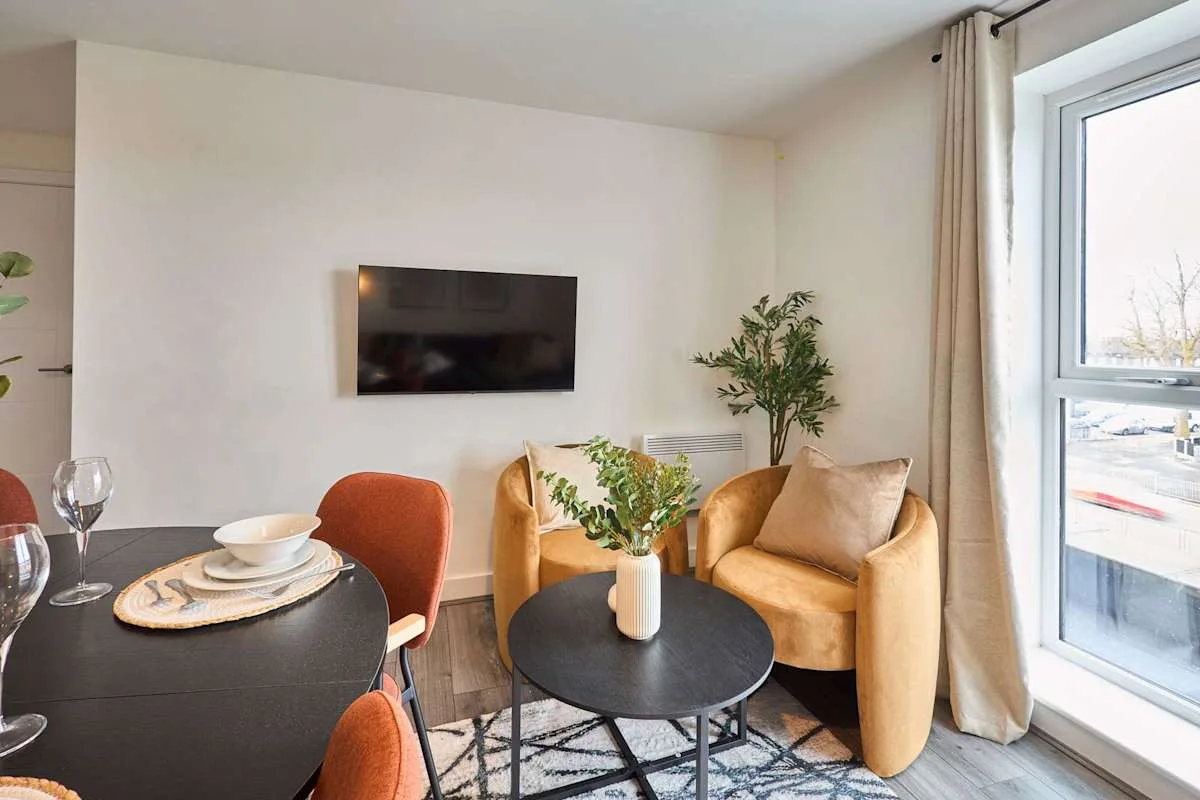 A living room with mustard-colored seating, a wall-mounted television, and a round coffee table.