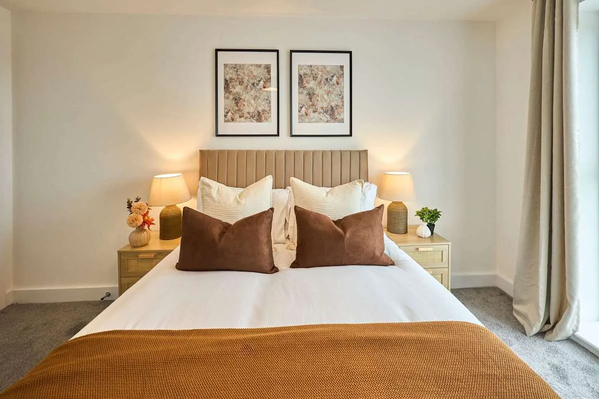 A bedroom with a neatly made bed, bedside tables, and framed artwork.