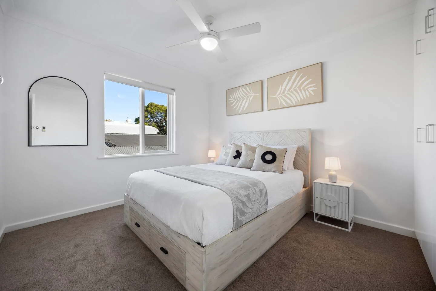 A bright bedroom with a bed, bedside tables, and framed botanical artwork.