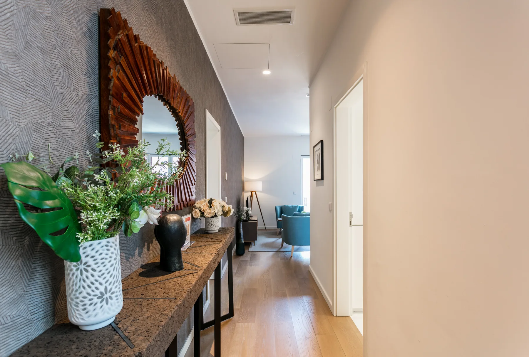 A furnished hallway with a console table, decorative mirror, and seating at the far end.
