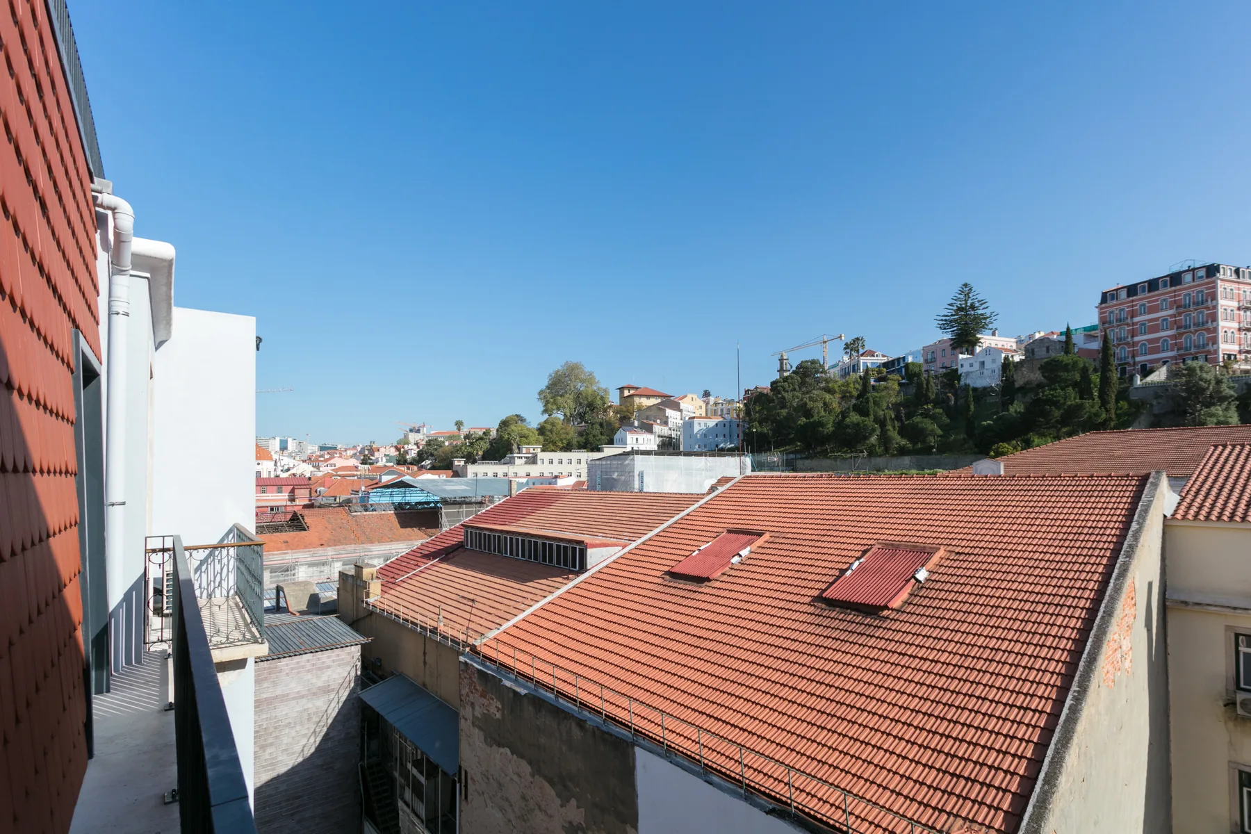 Rooftops and hillside buildings are visible from a balcony under a clear blue sky.