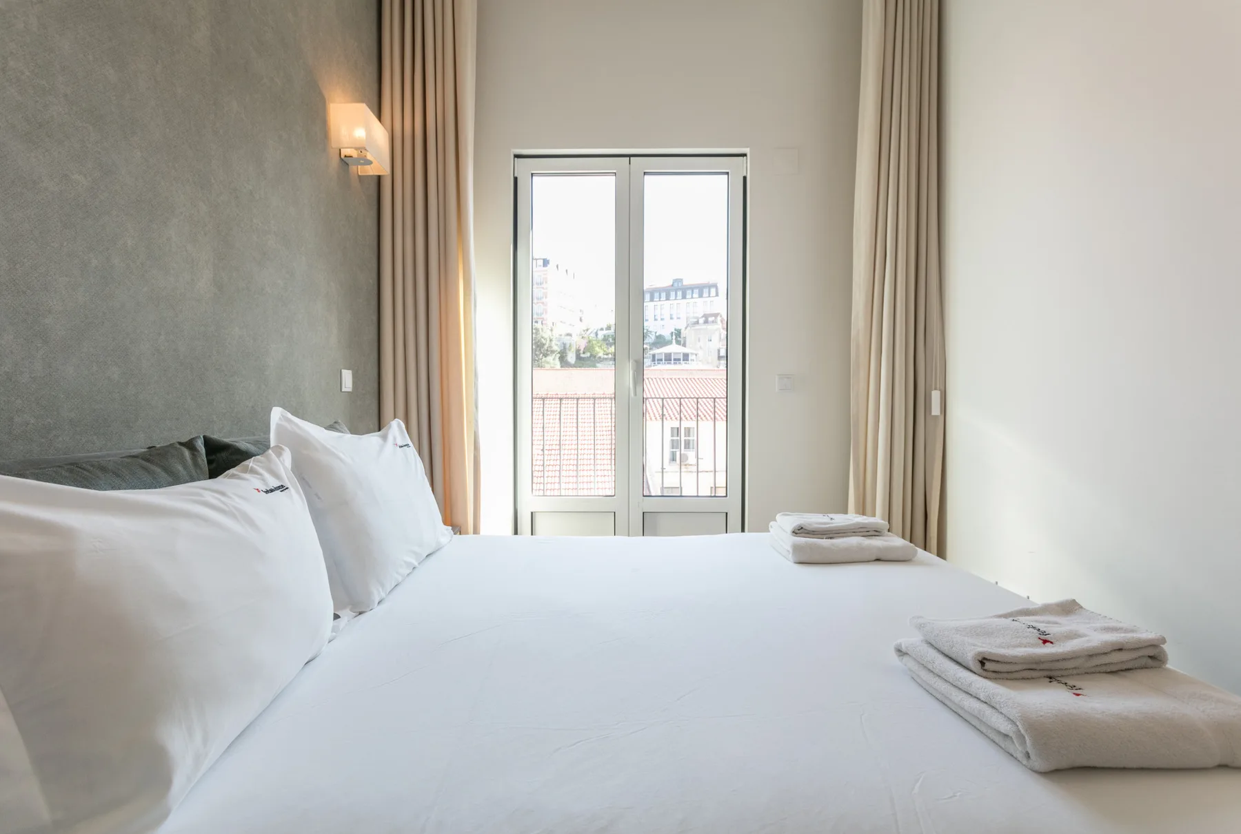 A bright bedroom with a neatly made bed and glass doors opening to a balcony.
