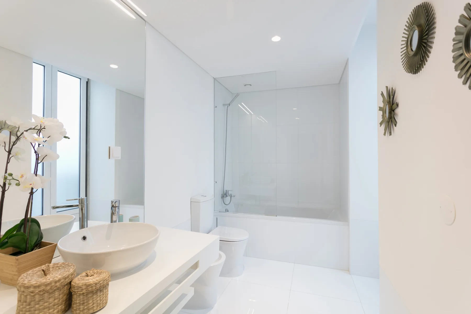 A bright bathroom with a sink vanity and a bathtub behind a glass screen.