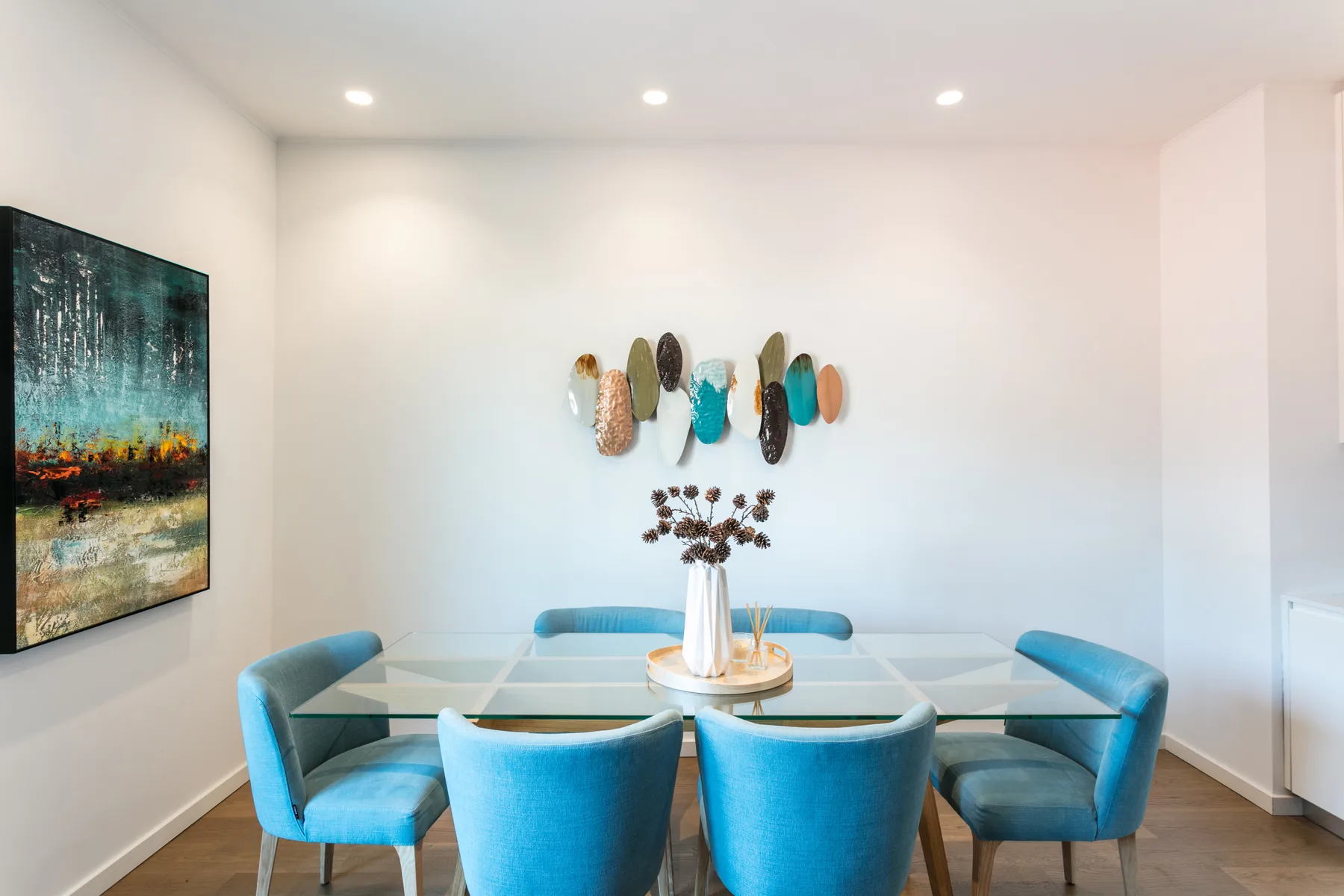 A dining area with blue seating around a glass table and colorful wall art.