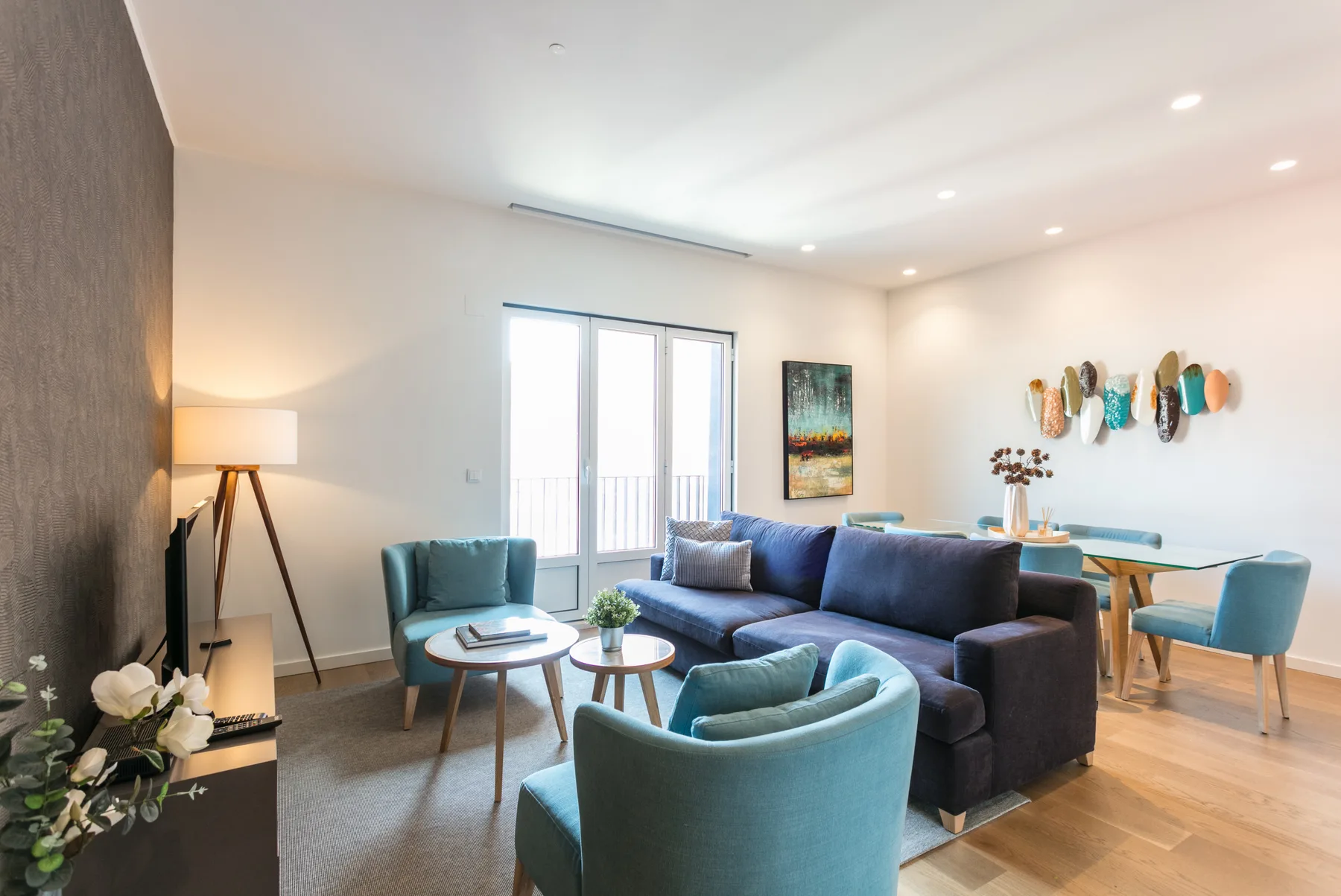 A bright living room with blue seating and a dining table by the windows.