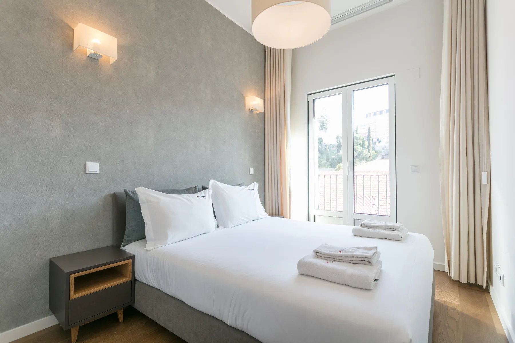 A bright bedroom with a neatly made bed beside a large window.