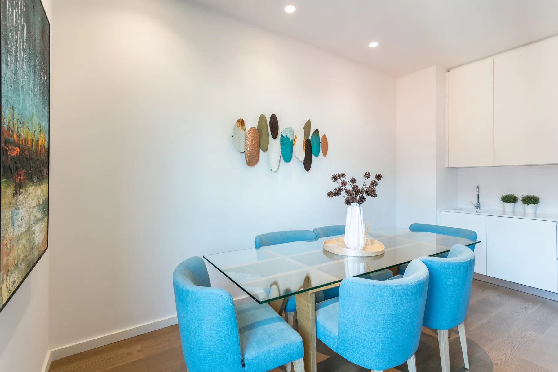 A dining area with a glass table, blue seating, and decorative wall art.