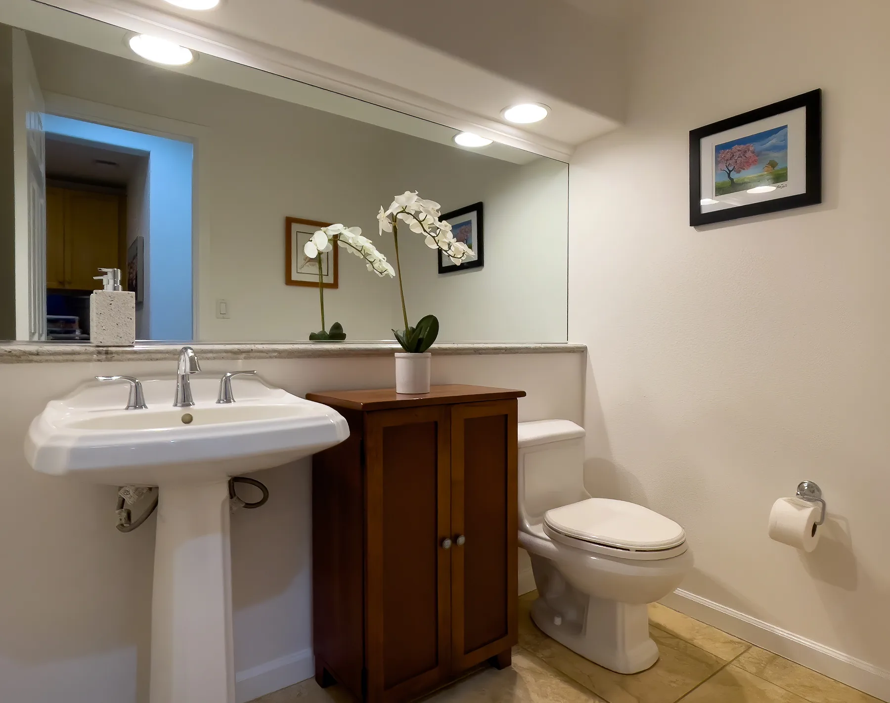 Un baño con lavabo, inodoro y un mueble de madera bajo un espejo grande.