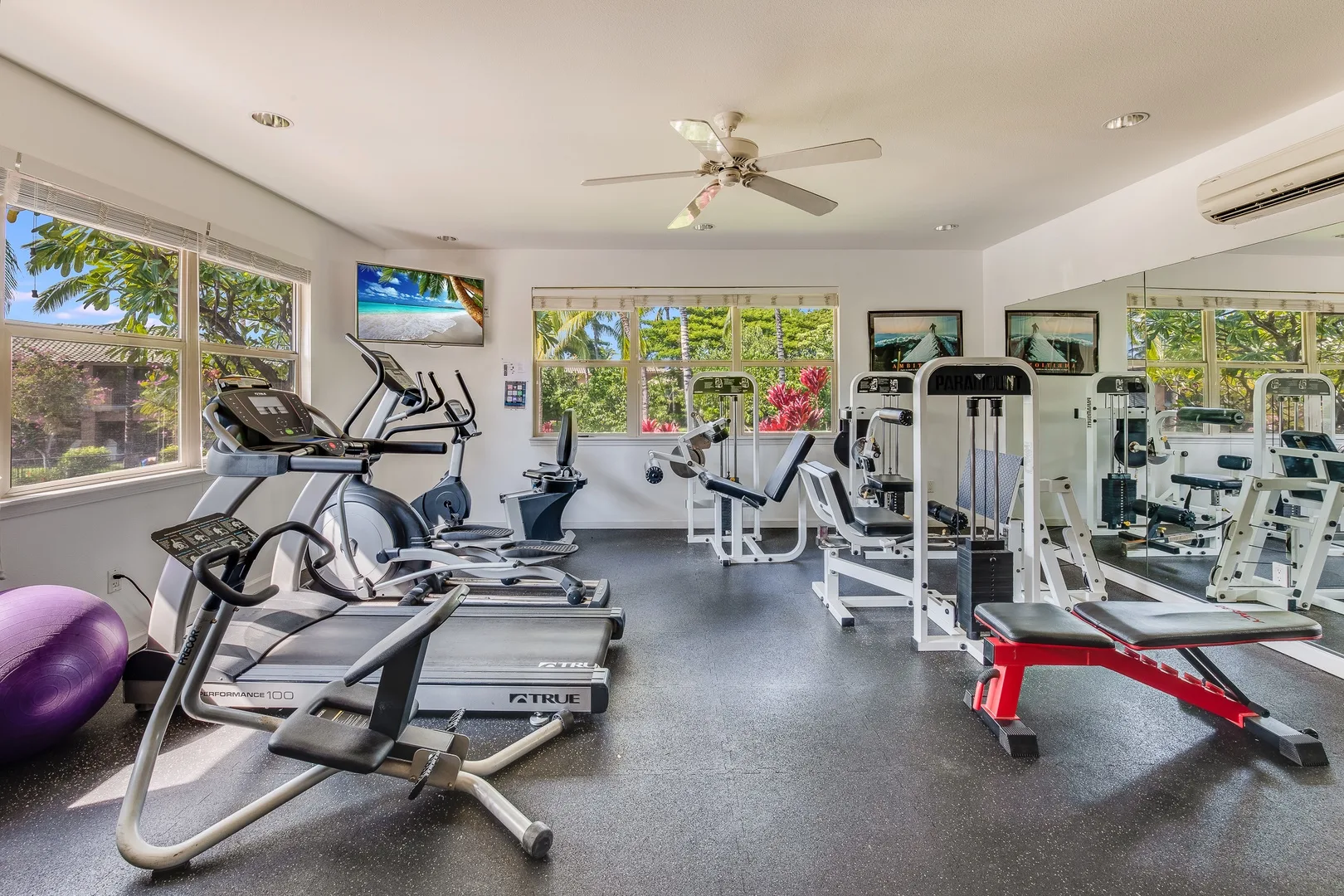 Un gimnasio con cintas de correr, máquinas de ejercicio y una pared de espejos.