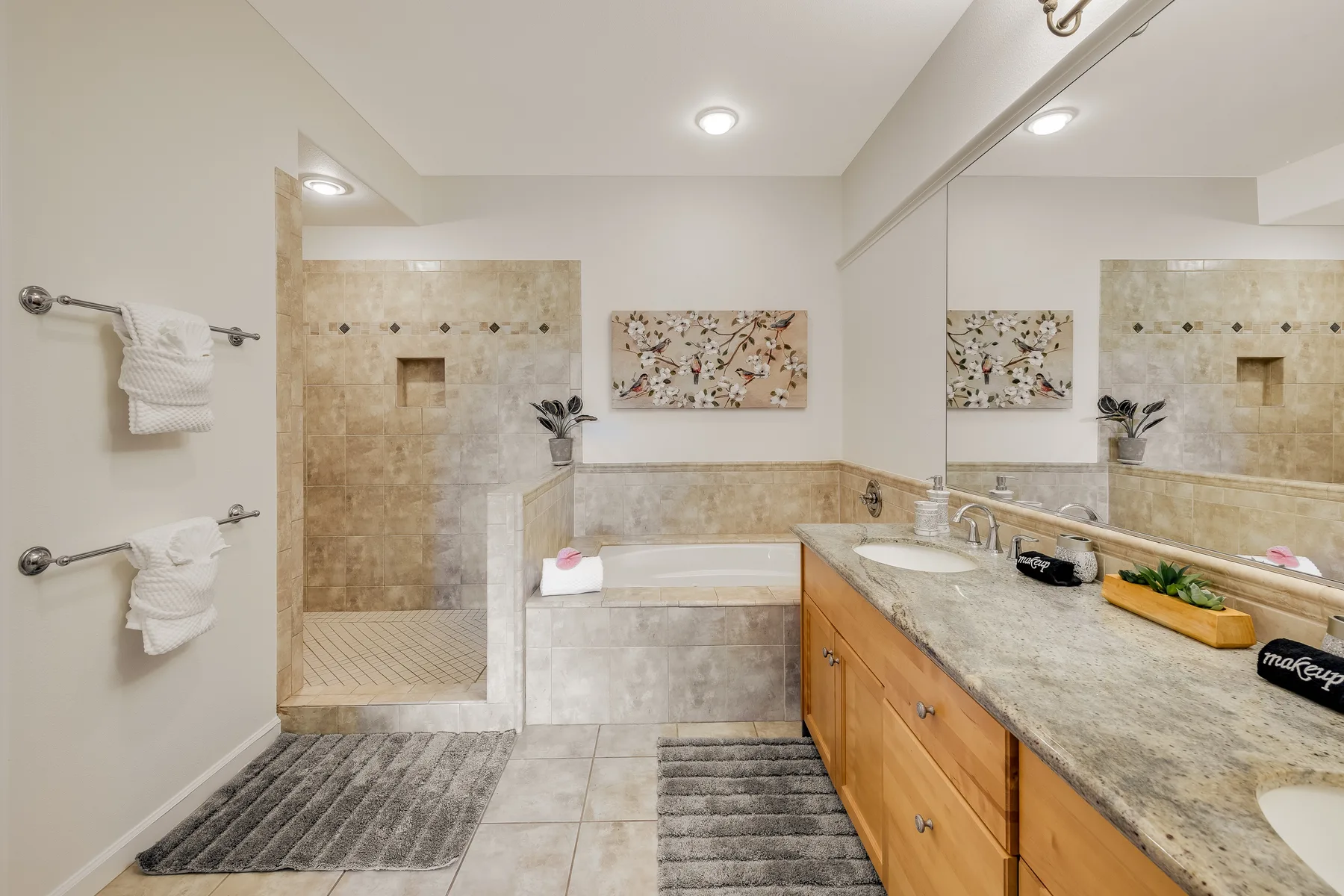 Un baño luminoso con una ducha de azulejos y un largo tocador bajo un espejo.
