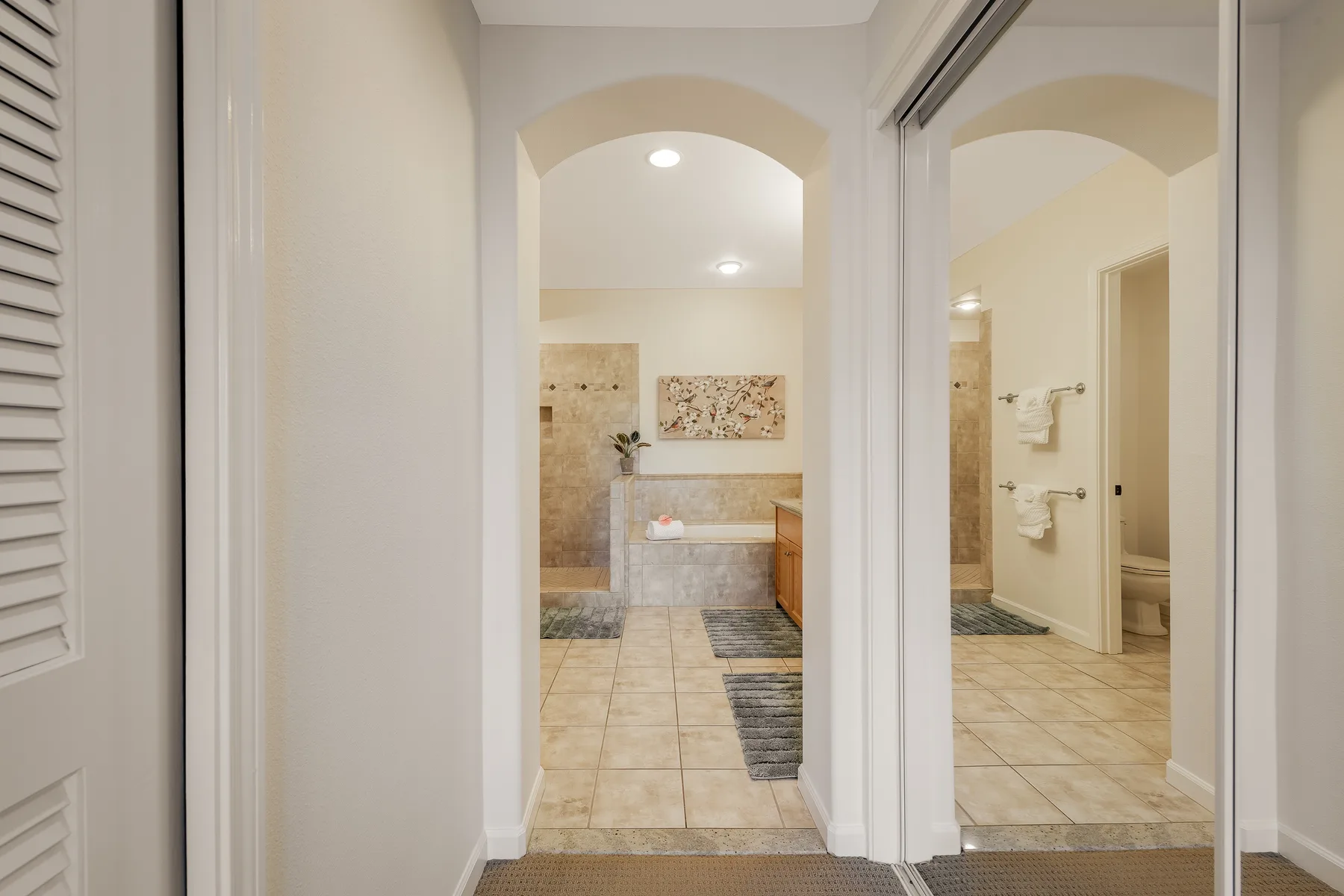 Se ve un baño con azulejos a través de un arco, con un gran espejo en la pared.
