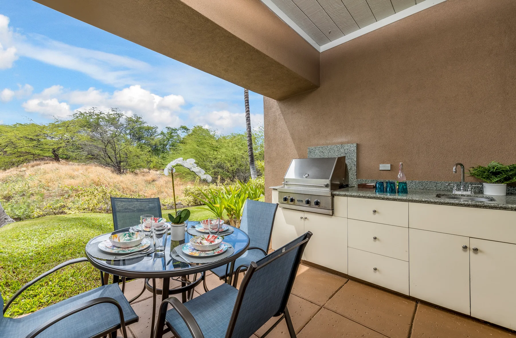 Comedor exterior cubierto con una mesa puesta junto a una parrilla empotrada.