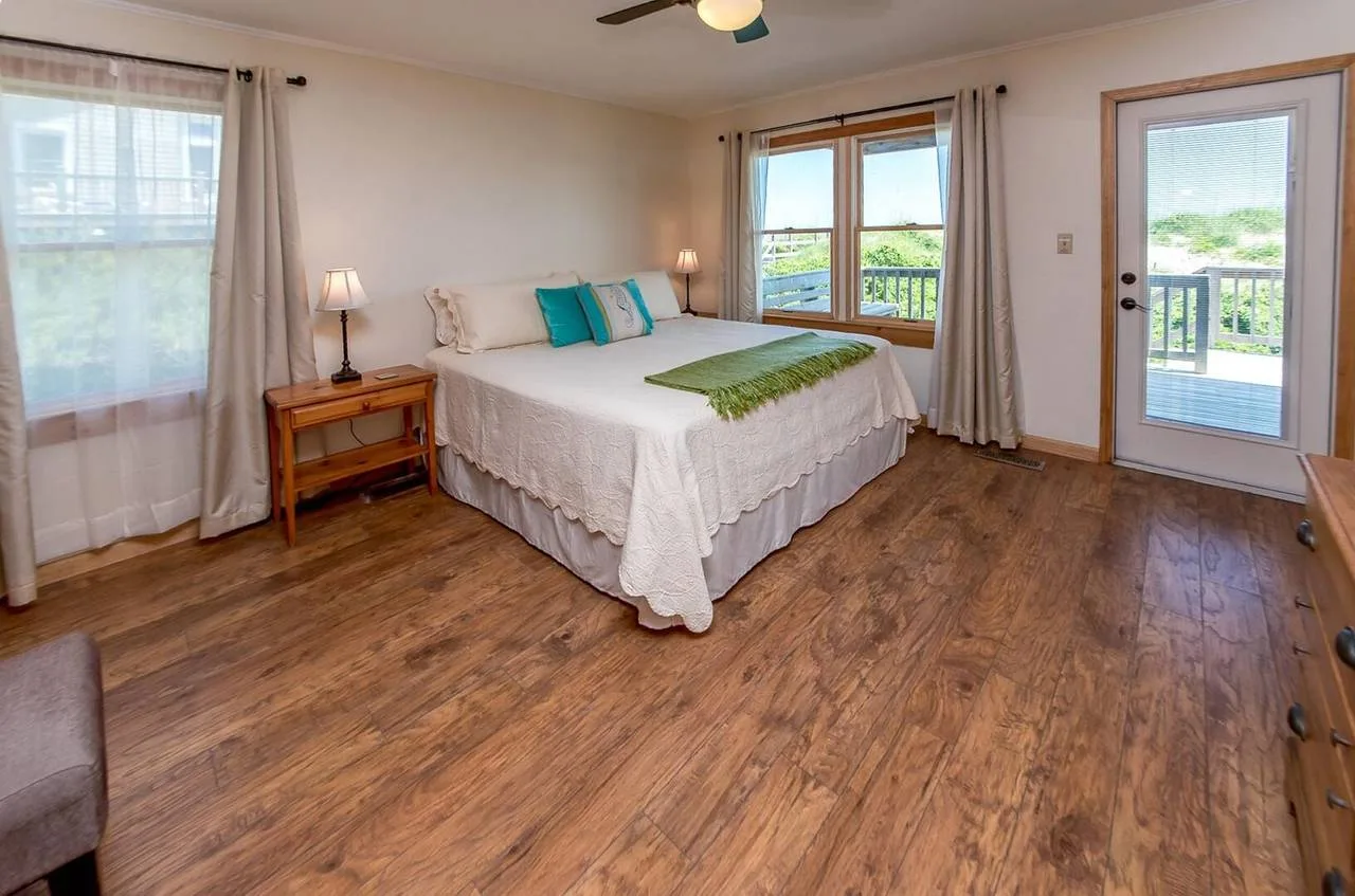 A bedroom with a bed, windows, and a glass door opening onto a balcony.