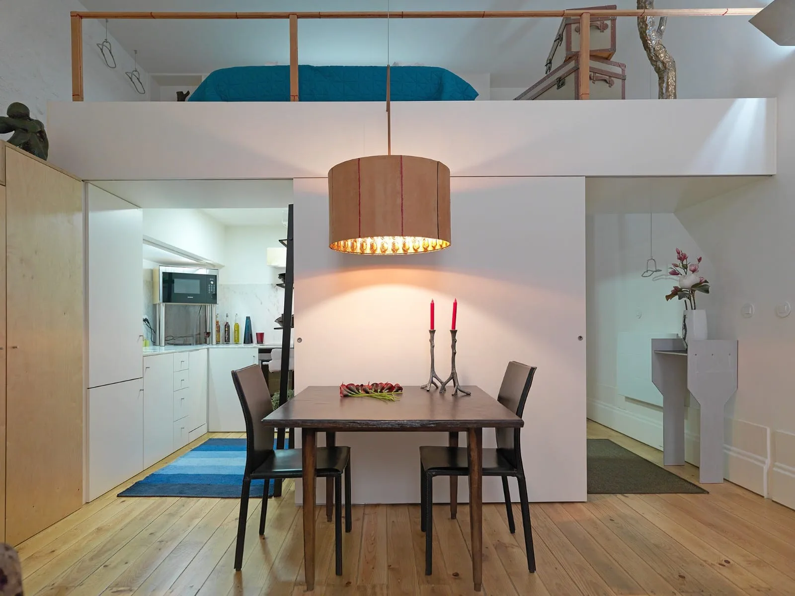 A dining area with a wooden table and chairs sits beneath a mezzanine.