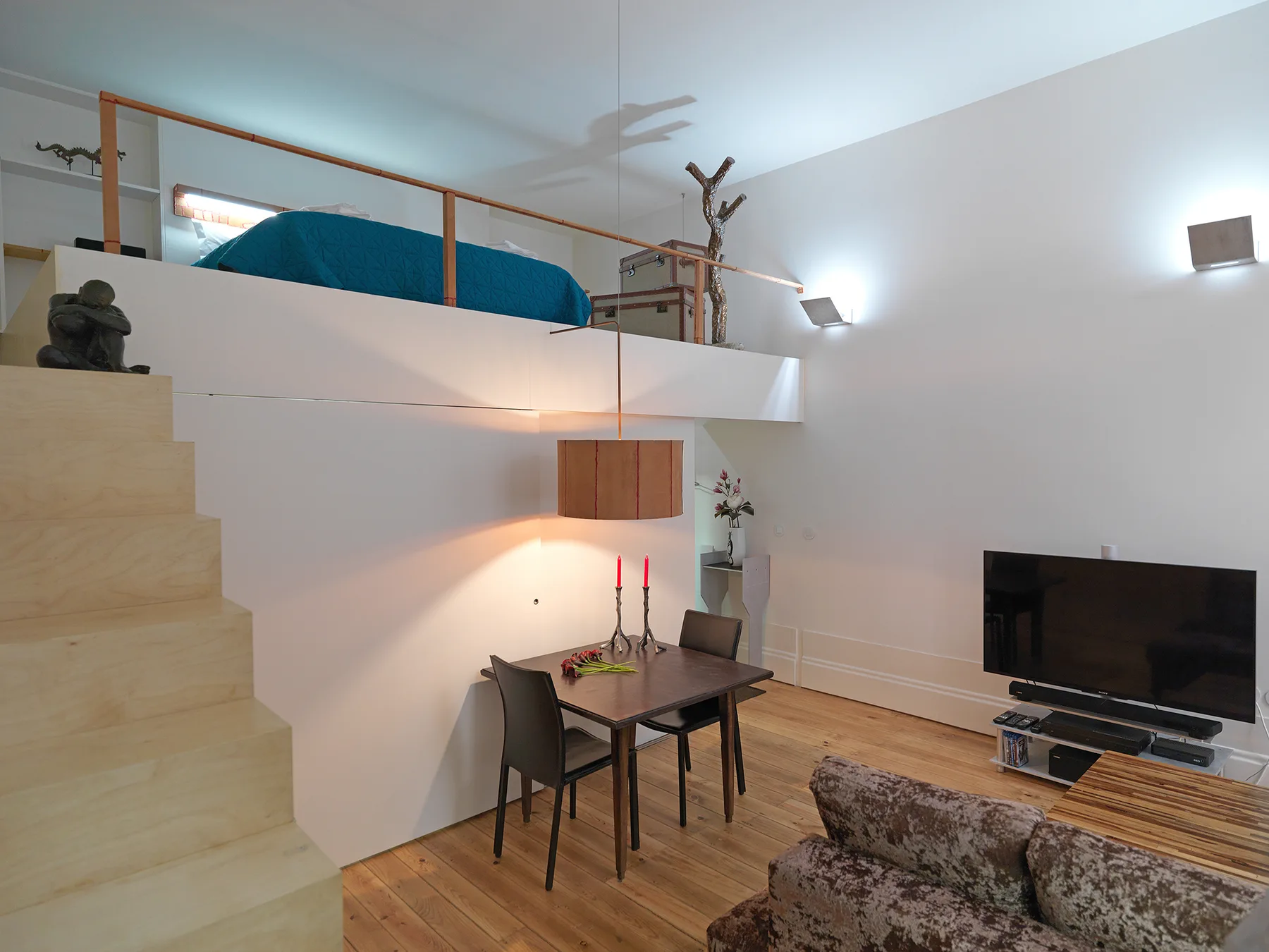 Una sala y comedor tipo loft con un espacio elevado para dormir y un televisor.