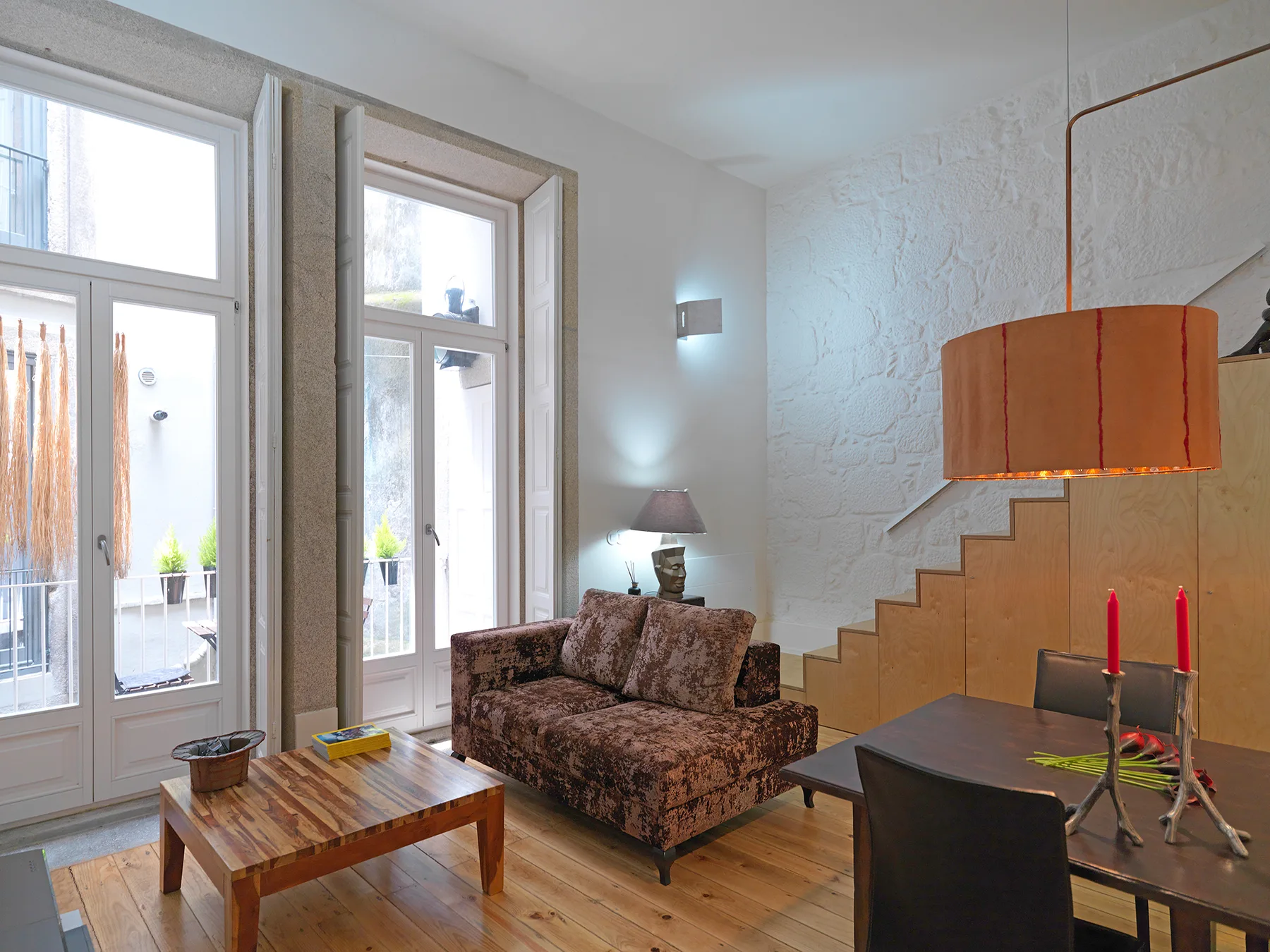 A living room with tall windows, patterned seating, and a staircase.