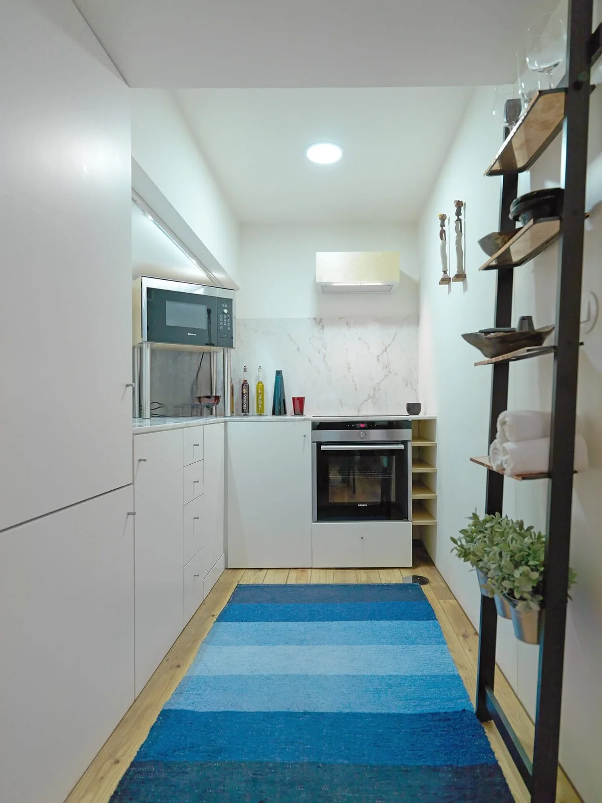 A compact kitchen with white cabinets, a countertop, and a blue striped rug.