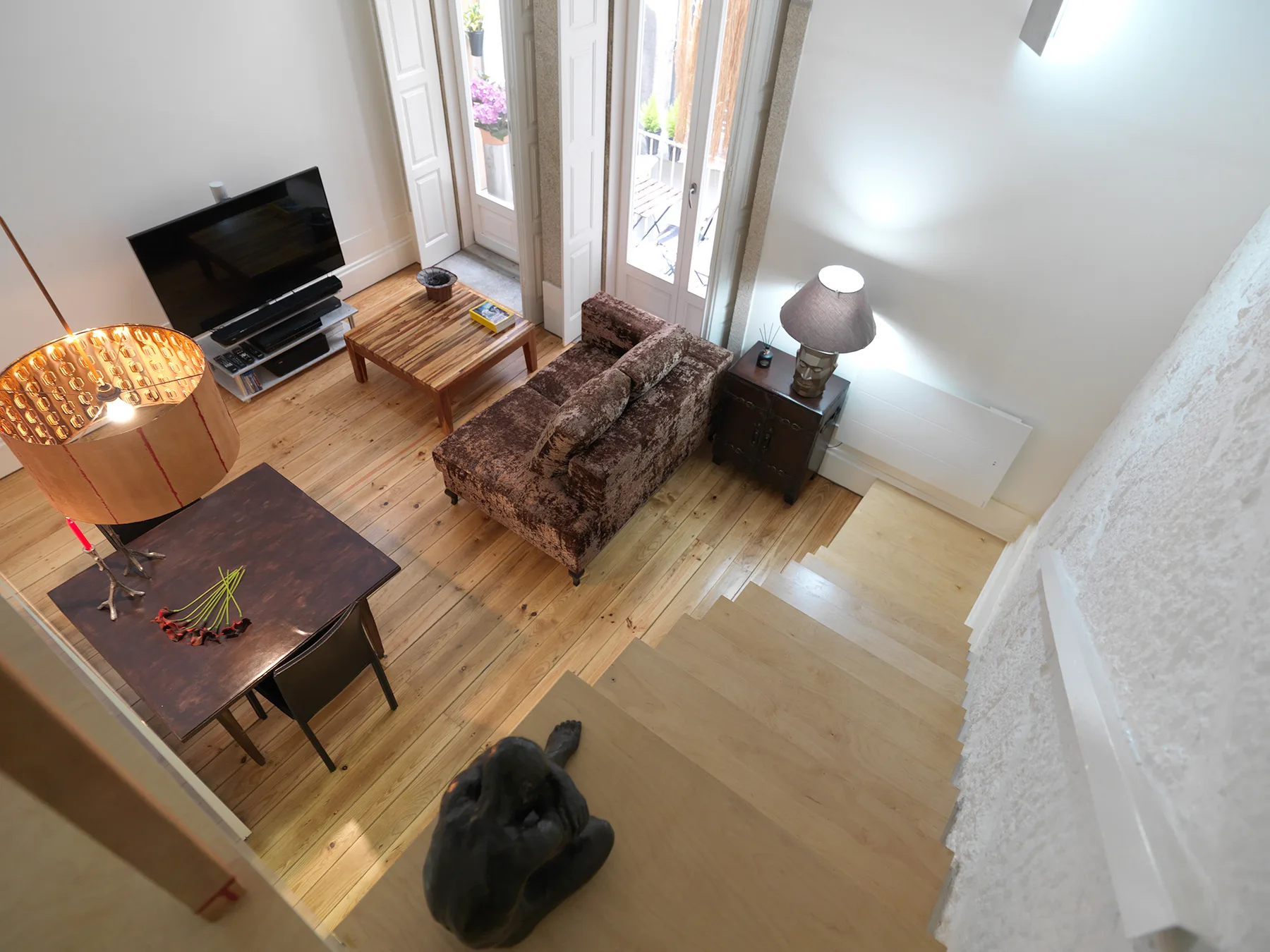 Una sala de estar con asientos, un televisor y ventanas altas que dan a un balcón.
