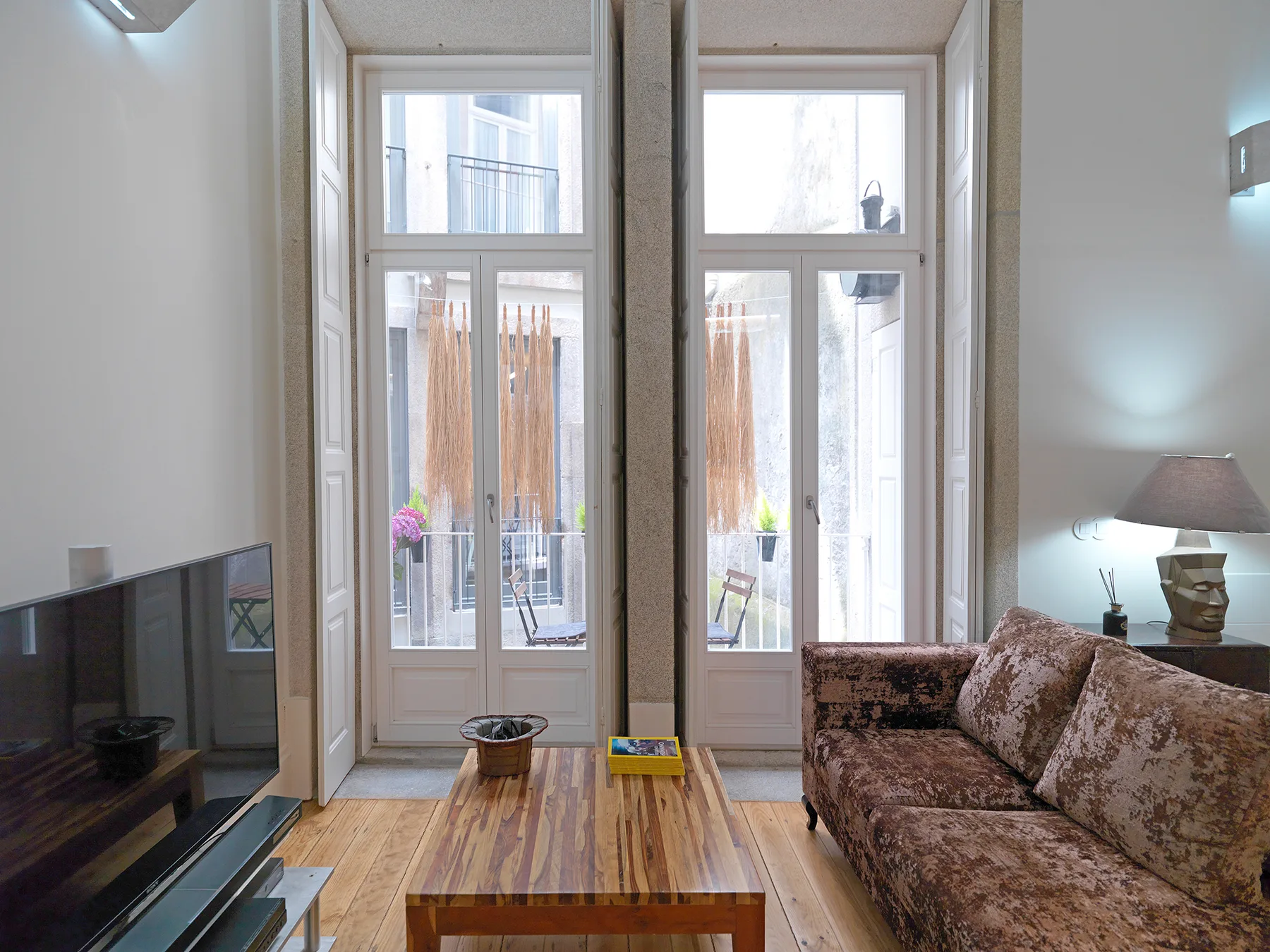 Una sala de estar con televisor, asientos y ventanas altas que dan a un pequeño patio.