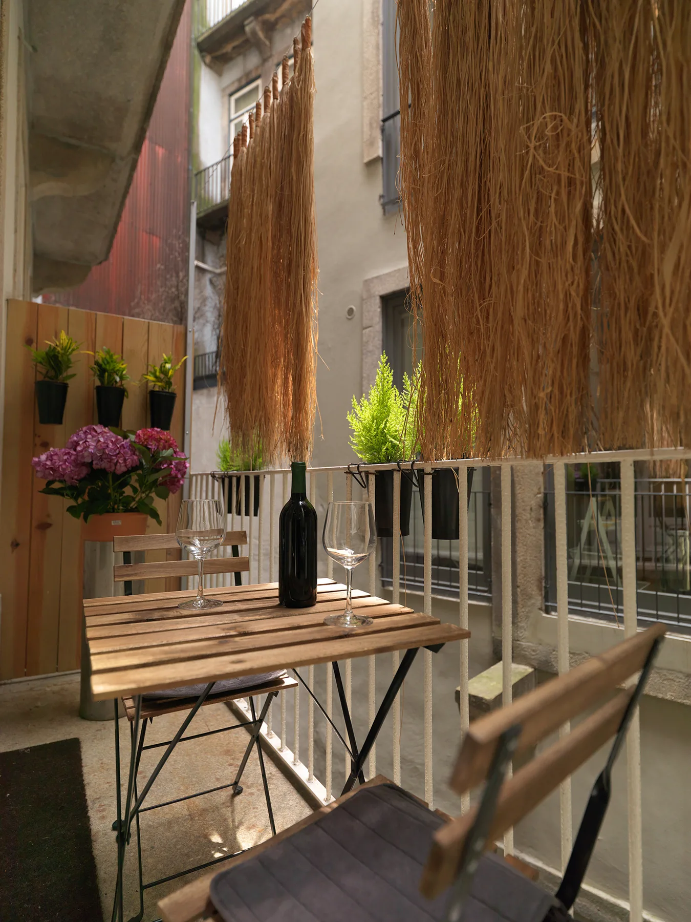 Un pequeño comedor exterior con una mesa de madera, sillas y plantas.