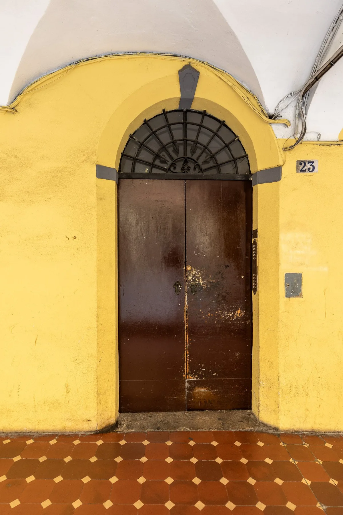 An arched dark wooden entrance set into a yellow wall above a patterned tile floor.