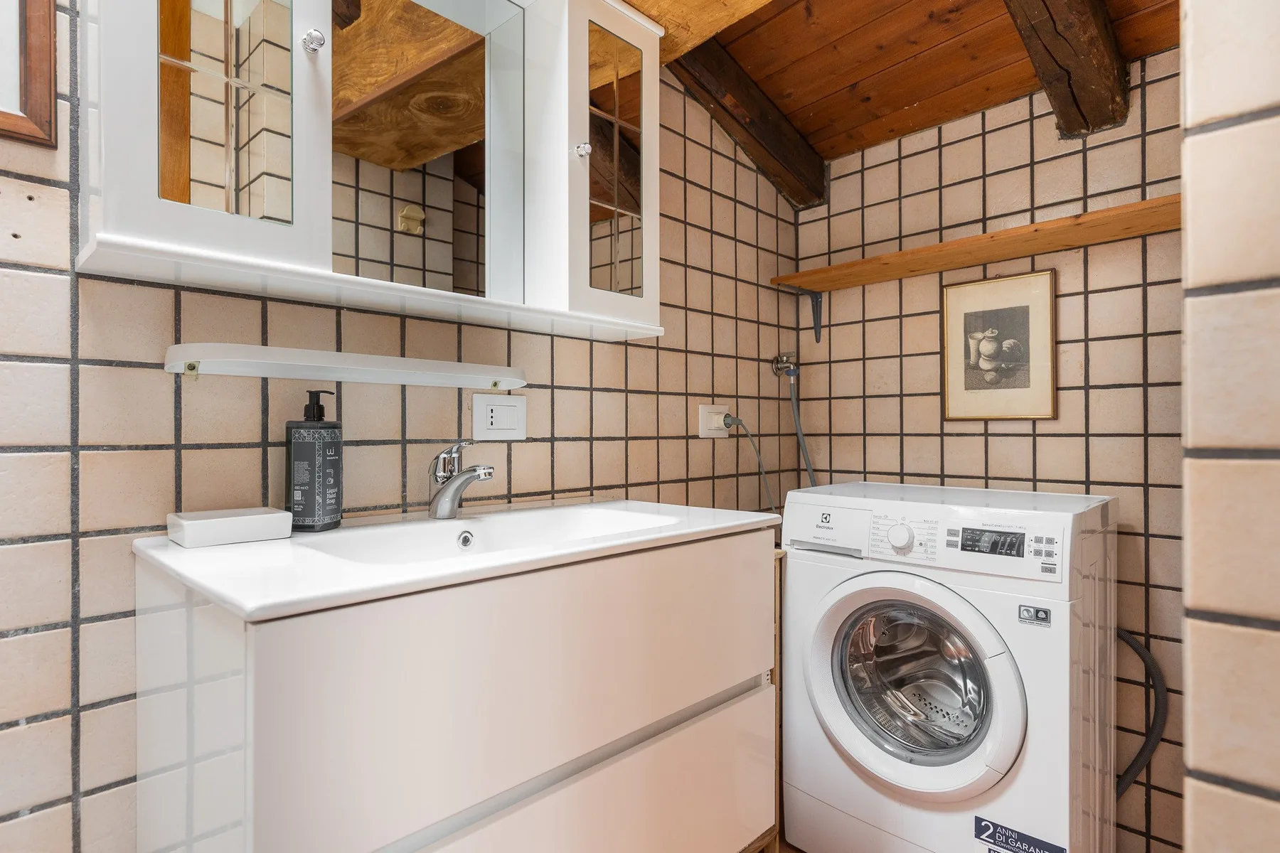 A tiled bathroom with a sink, mirrored cabinets, and a washing machine.