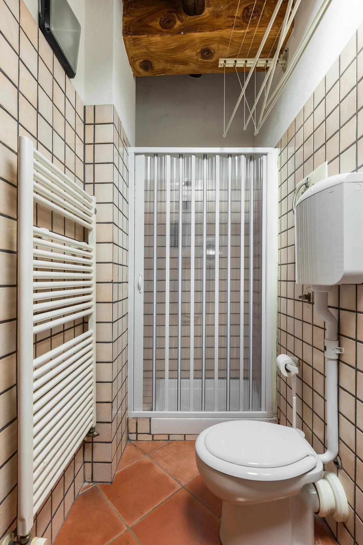 A tiled bathroom with a toilet, radiator, and shower behind a glass screen.