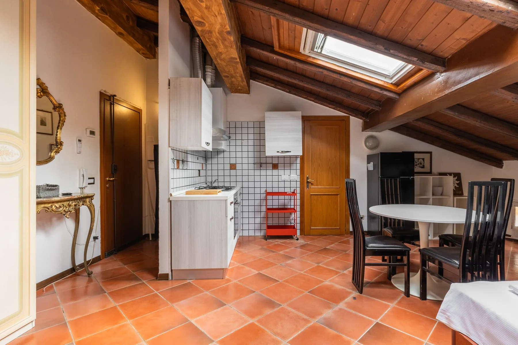 A dining and kitchen area beneath a sloped wooden ceiling, with a skylight overhead.