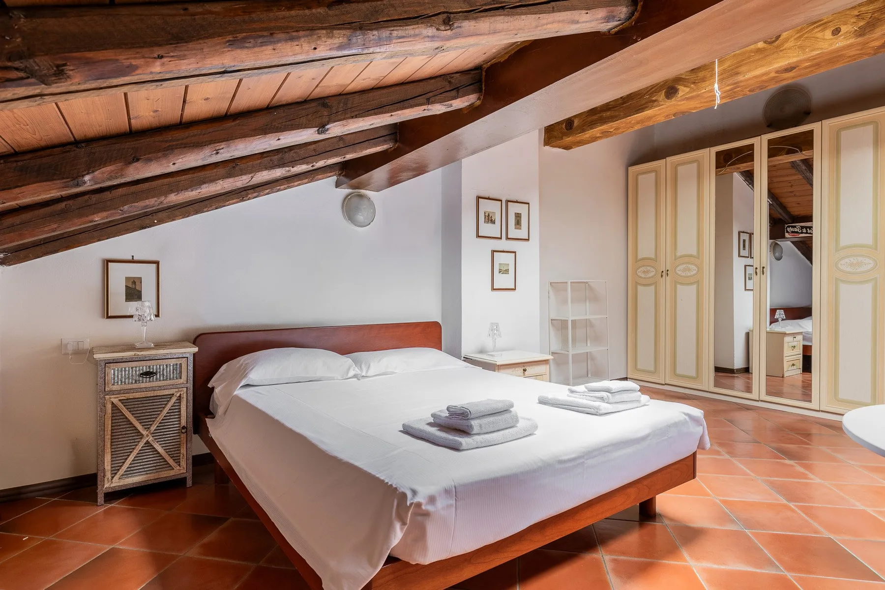 A bedroom with a bed beneath a sloped wooden-beam ceiling.