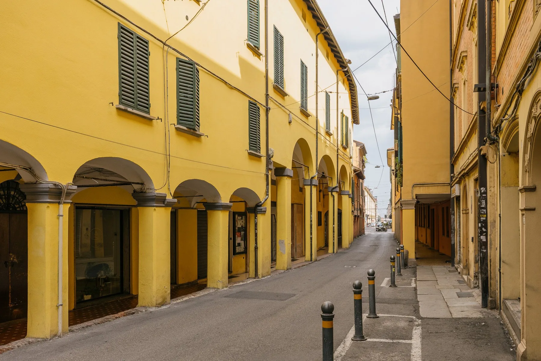 A narrow street runs between yellow buildings with arched ground-floor walkways.