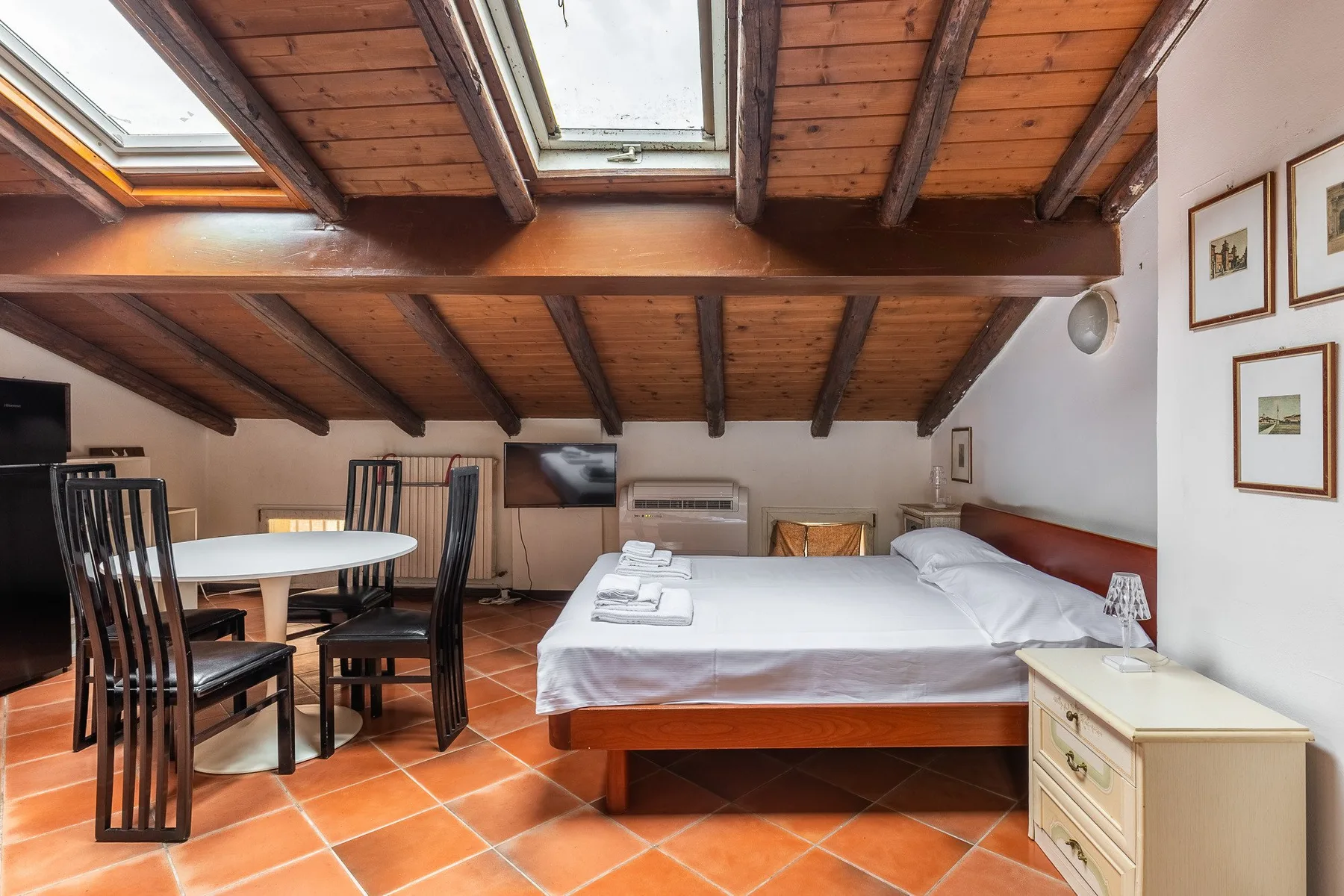 A bedroom with a large bed, a small dining table, and skylights.