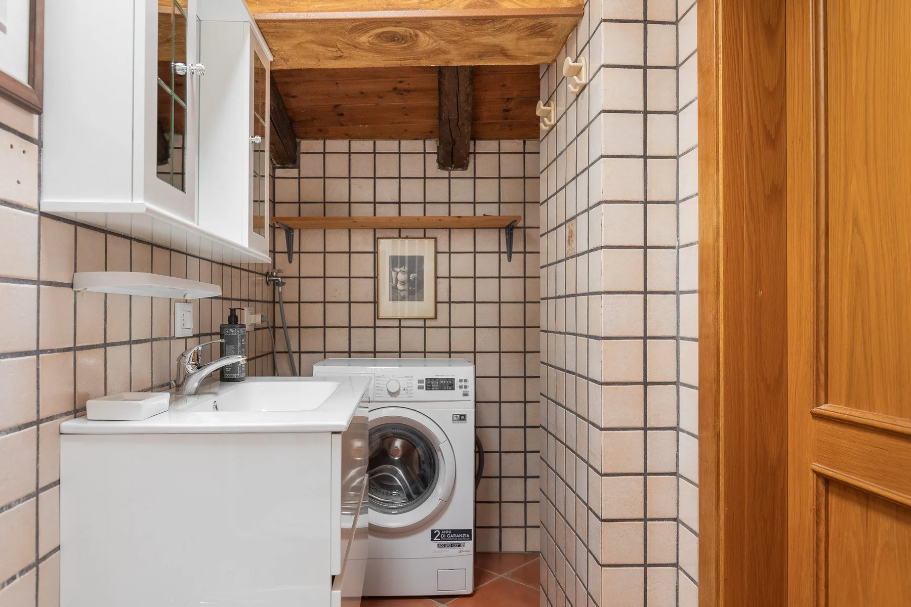 A tiled bathroom with a sink, washing machine, and wooden door.