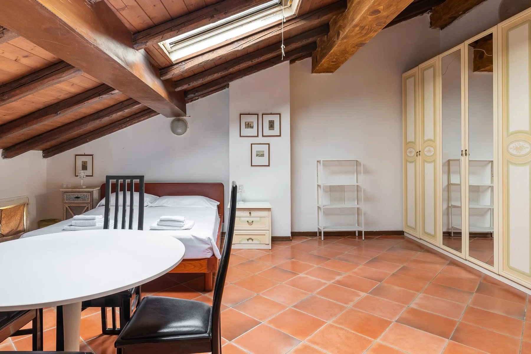 A bedroom with a bed, a table, and a sloped timber ceiling.