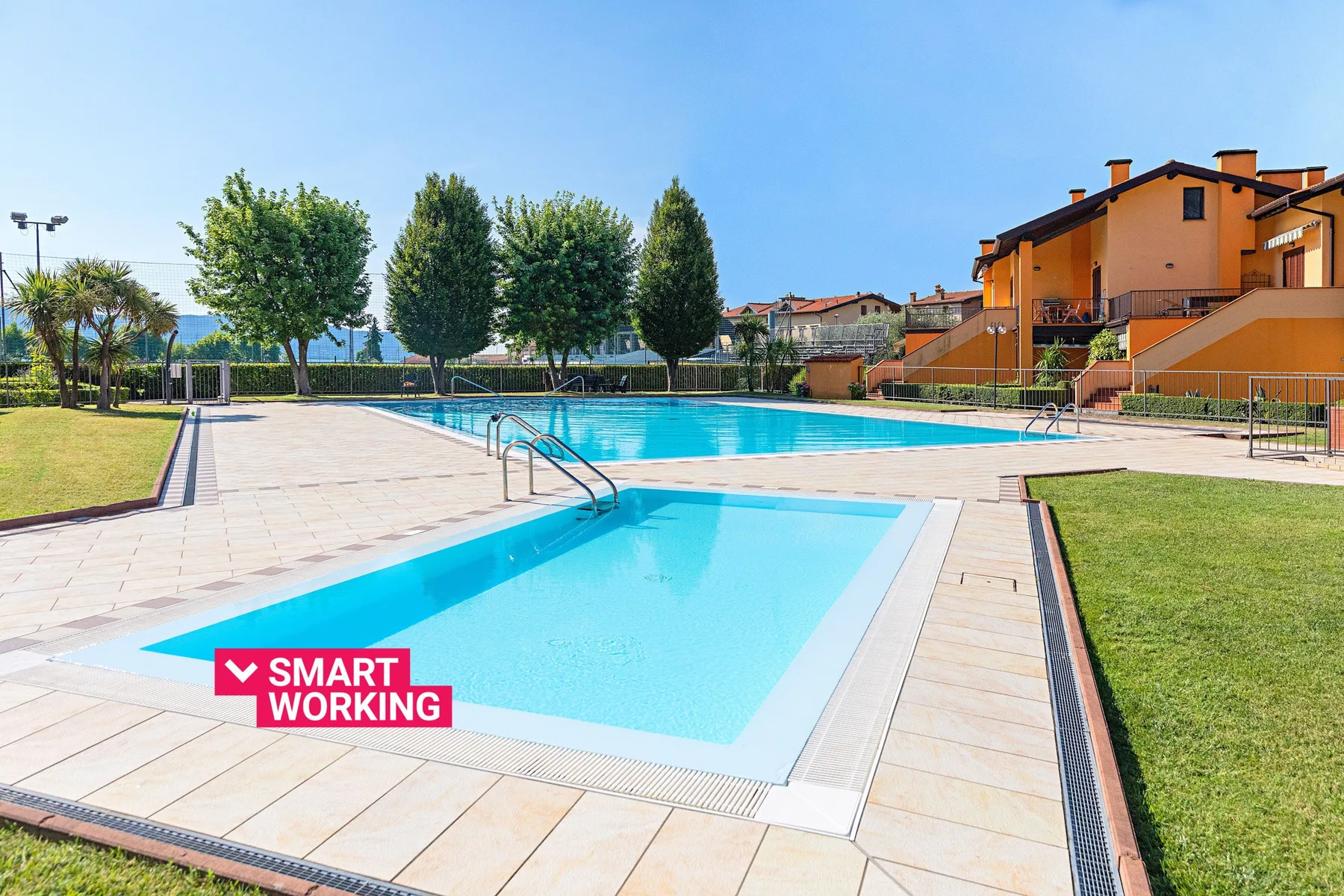 An outdoor swimming pool with a smaller adjoining pool beside orange buildings.