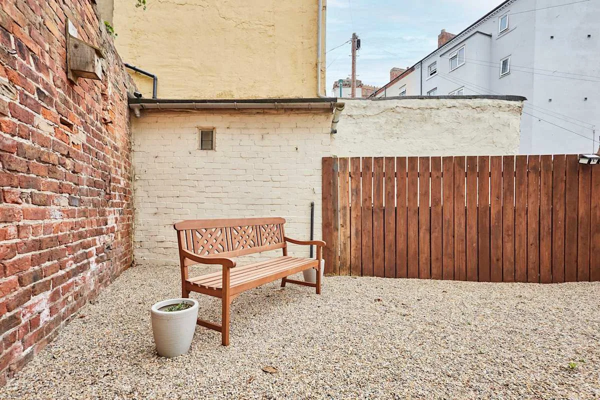 Un patio de grava con un banco de madera junto a paredes de ladrillo y pintadas.