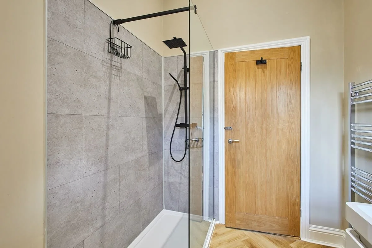 Un baño con ducha, mampara de vidrio y puerta de madera.