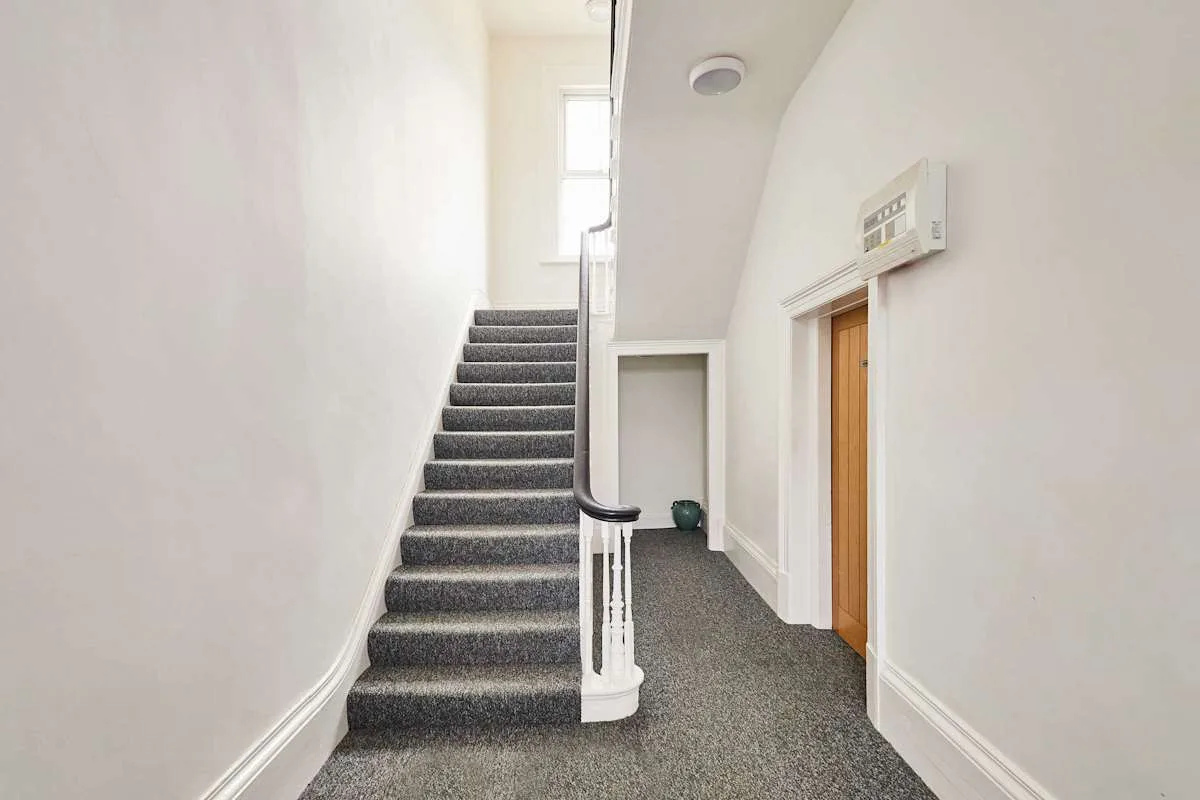 Un pasillo interior con una escalera alfombrada y una puerta.
