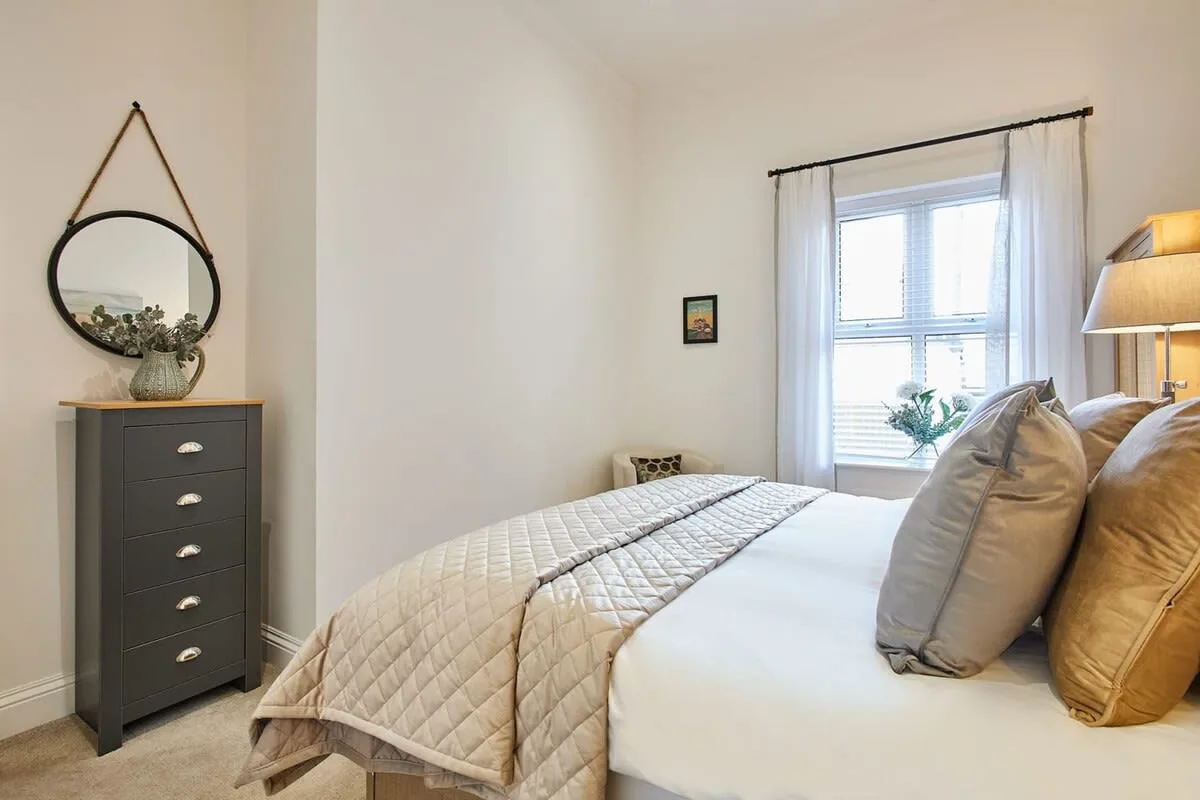 A bedroom with a neatly made bed and a dresser beside the window.