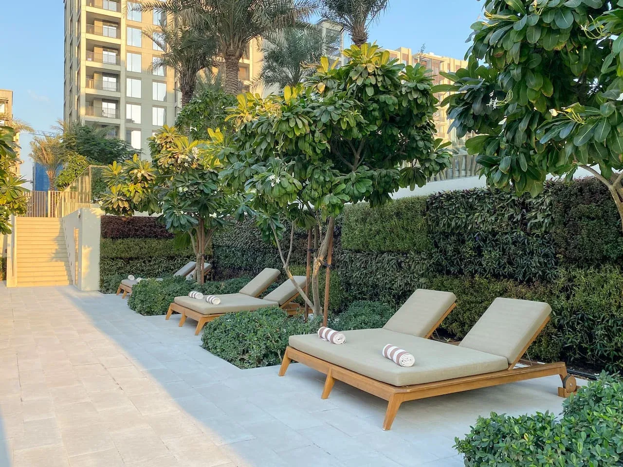 Asientos al aire libre junto a la piscina bajo árboles frondosos y junto a un sendero ajardinado.