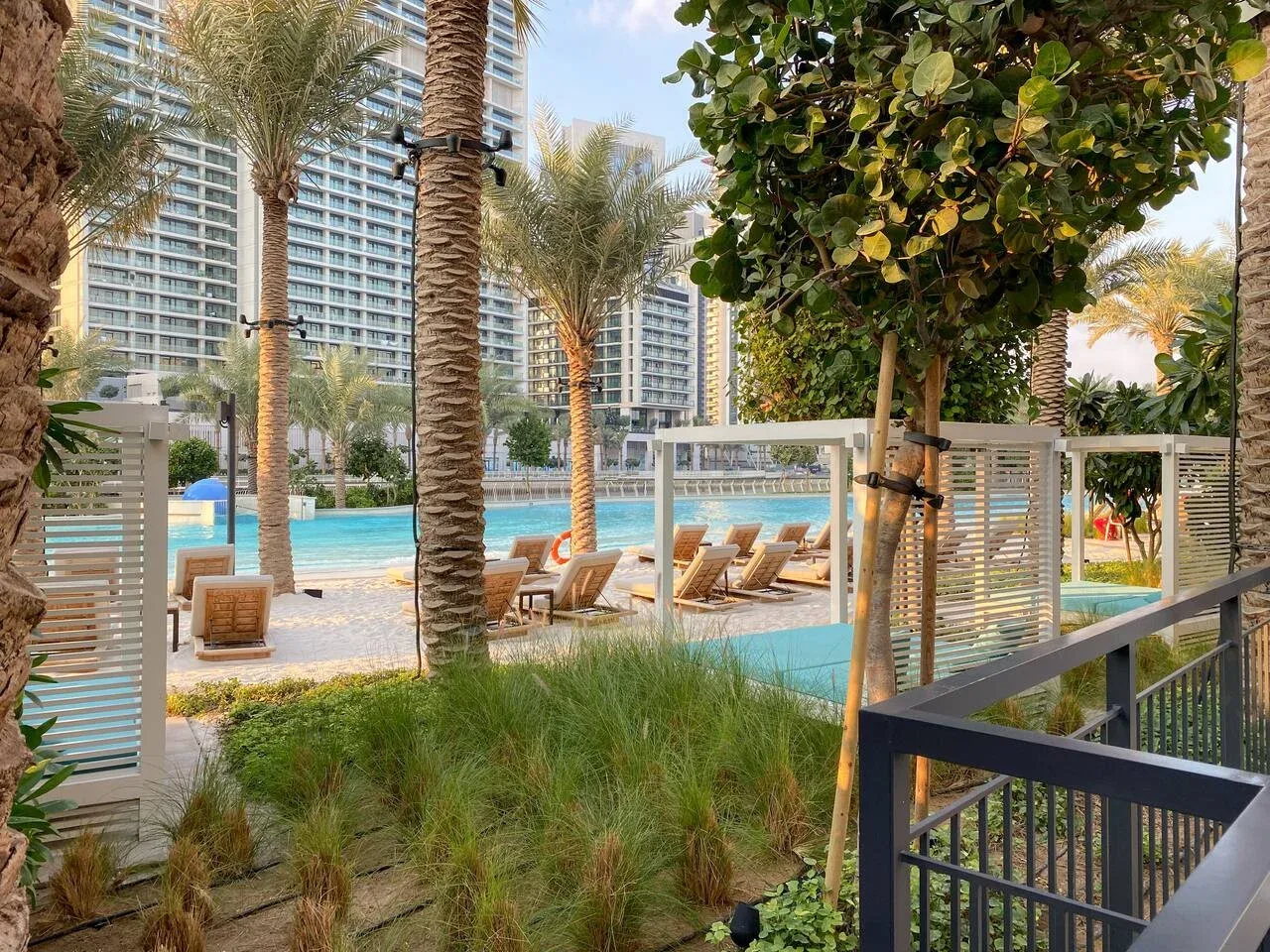 Una zona de piscina ajardinada con asientos, palmeras y edificios altos.