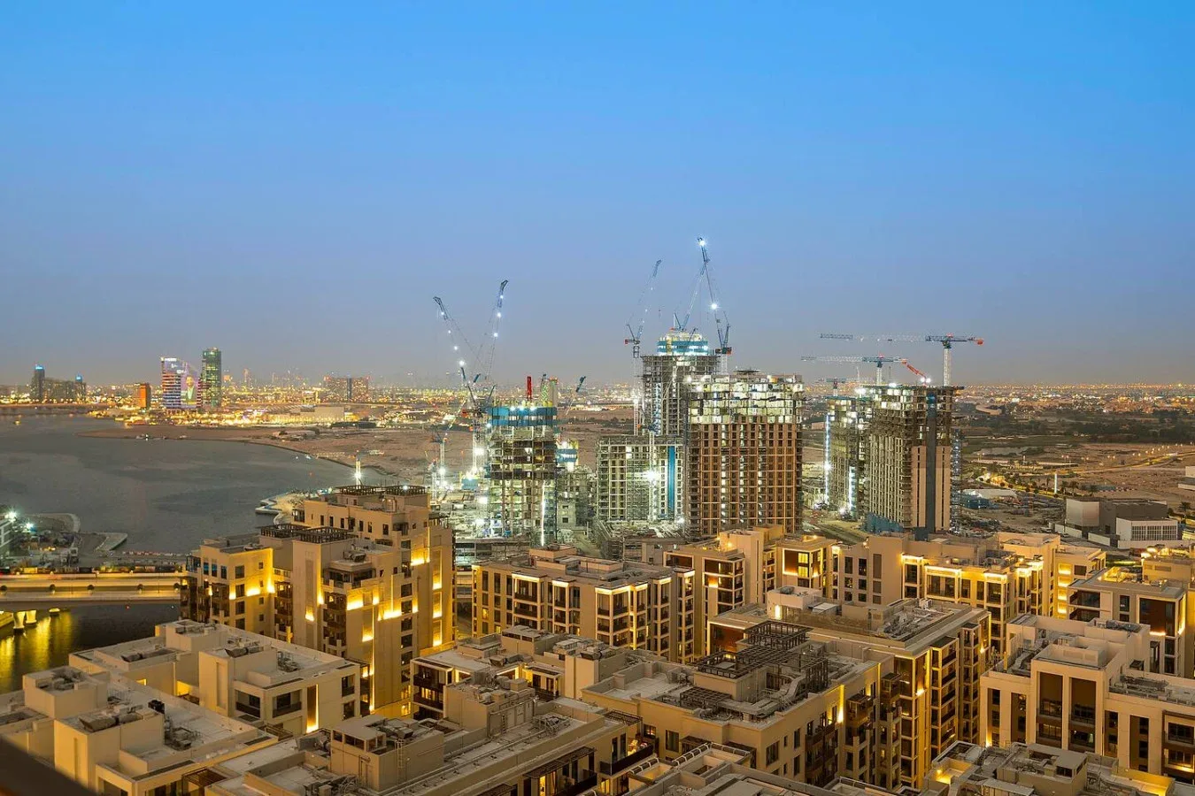 Un horizonte urbano al anochecer con edificios iluminados y grúas de construcción.
