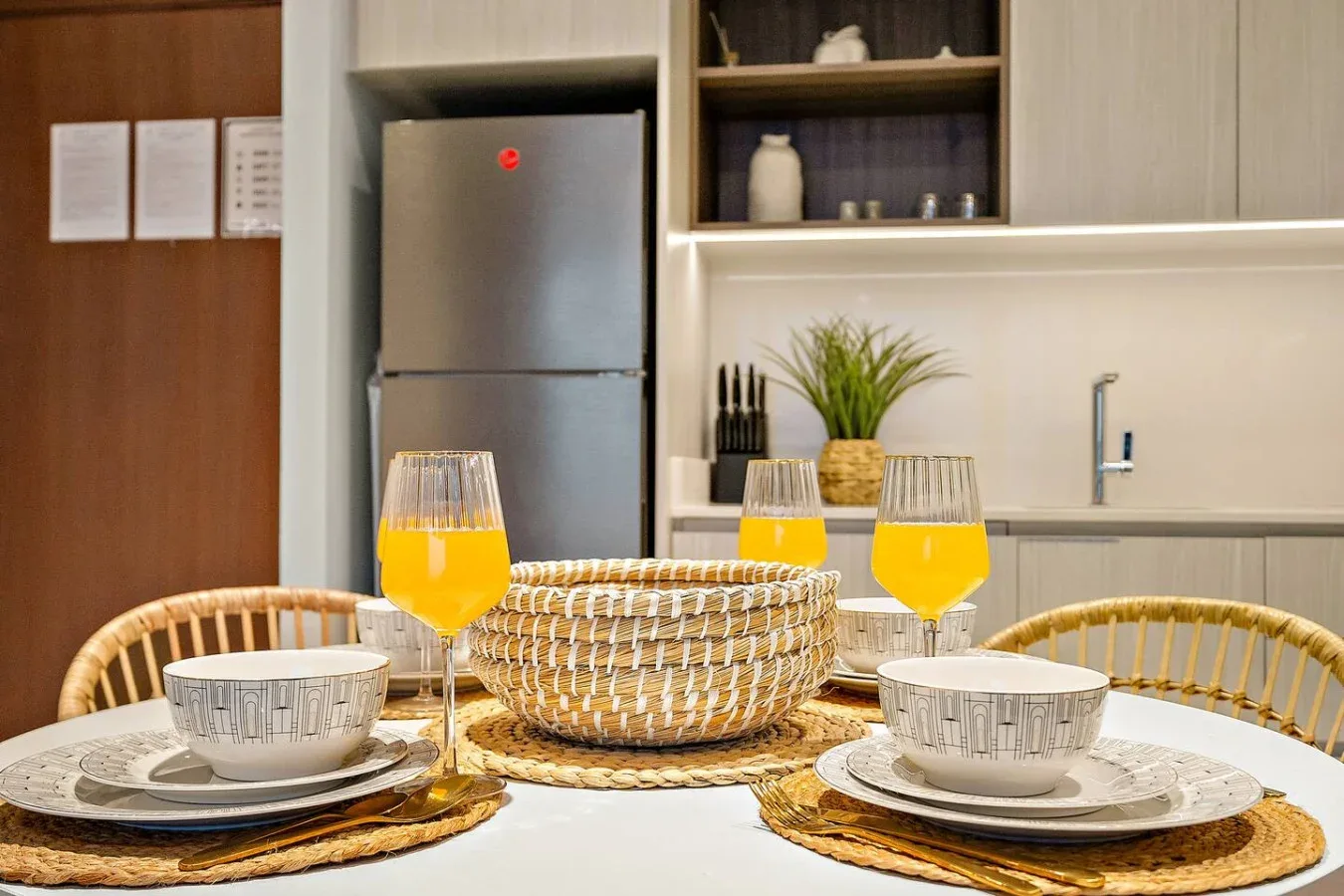 Una mesa puesta con zumo de naranja está frente a una cocina.