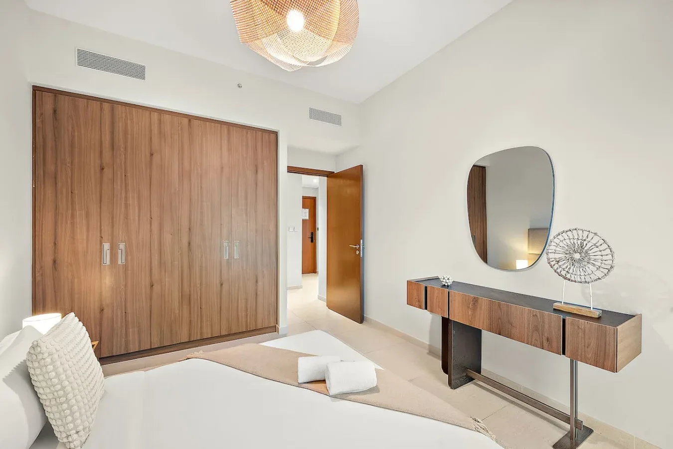 Un dormitorio luminoso con un gran armario de madera y un tocador bajo un espejo.